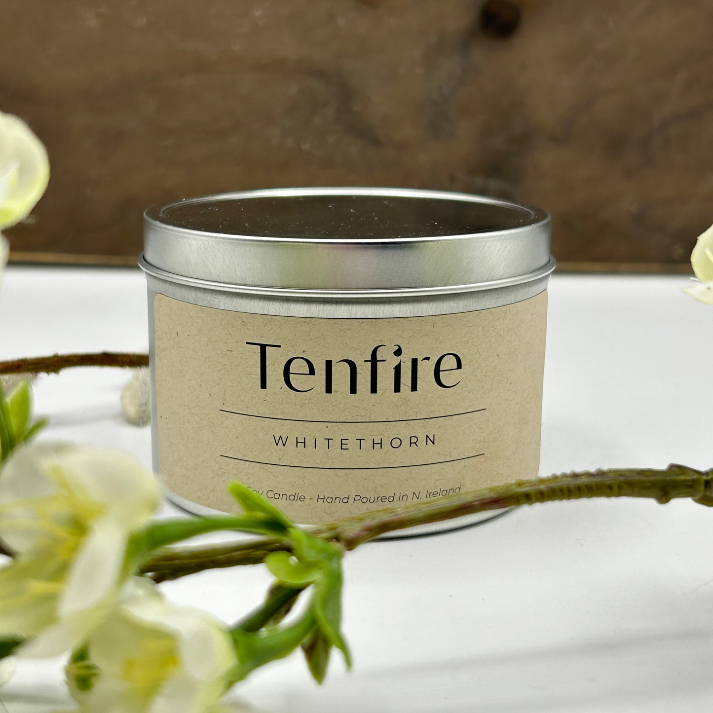 soy wax candle tin called Whitethorn, next to a hawthorn flower in front of wooden board